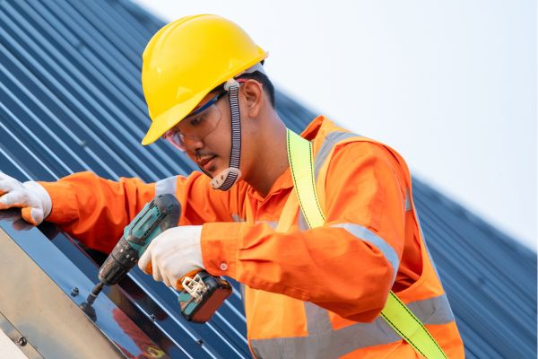 Roofer Installing A New Roof Using A Drill To Fix Roof Metal Sheets